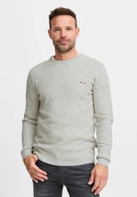 Pull gris clair avec un design en tricot texturé, col rond et poignets côtelés. Petit logo coloré sur la poitrine.