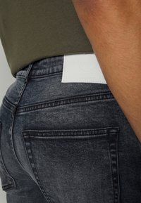 Slim-fit, vybledlé černé džíny s hladkou texturou. Na zadním pásku se nachází bílá kožená visačka se značkou "DENIM PROJECT".