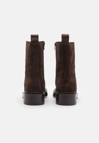 Bruna mockasuede ankelboots med en slät svart sula, sidoglittrar och tyghandskar baktill för enkelt påtagande.