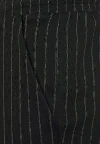 Tissu noir avec un motif à rayures verticales grises, présentant une surface texturée et une coupe ajustée, incluant un détail de couture sur le côté.