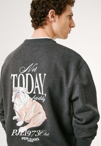 Sudadera gris oscuro con una ilustración de un bulldog y el texto "No HOY, amigo" en blanco y rosa. Cuello y puños acanalados.
