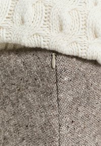 Tissu en crème tricoté avec un motif en câble sur le dessus, superposé à un tissu brun texturé avec un détail de fermeture éclair sur le côté.