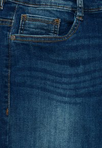 Jeans de mezclilla con un lavado azul oscuro, con costuras naranjas, un bolsillo frontal y una textura suave. La tela muestra un ligero desgaste.