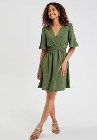 Robe verte à manches courtes avec un décolleté en V, taille froncée et jupe évasée. Fabriquée dans un tissu texturé avec une coupe décontractée.