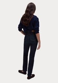Haut à manches longues navy, jeans bleu foncé taille haute avec poches arrière, texture lisse, et patch en cuir marron à la taille.