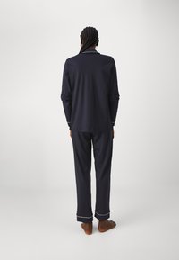 Marinblå pyjamasset i mjukt tyg, med långärmade tröjor och byxor med vita detaljer vid ärmslut och krage. Sedd bakifrån.