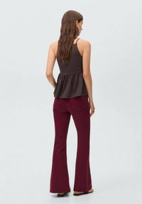 Débardeur peplum marron à fines bretelles associé à un jean bordeaux évasé. Tissu doux, design épuré et détails arrière remarquables.