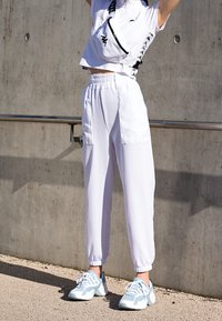 Vit kortärmad topp med korta ärmar, kombinerad med vita tapered joggers med framfickor, och ljusblåa träningsskor.