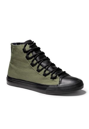 Wysokie sneakersy z oliwkowo zielonymi materiałowymi bokami, czarnym gumowym noskiem, podeszwą, językiem i grubymi czarnymi sznurowadłami na białym tle.