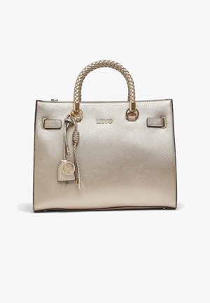 Sac à main en cuir doré métallisé avec poignées tressées, anneaux dorés et breloque à glands tressés suspendue ornée d'un médaillon rond avec logo.