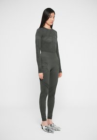 Maglietta lunga aderente verde scuro e leggings con motivi testurizzati. Abbinati a scarpe lucide argentate con punta a cono.