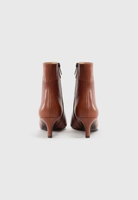 Bottines en cuir marron au design élégant, avec un talon effilé, des zips latéraux et une finition lisse, sur un fond blanc.