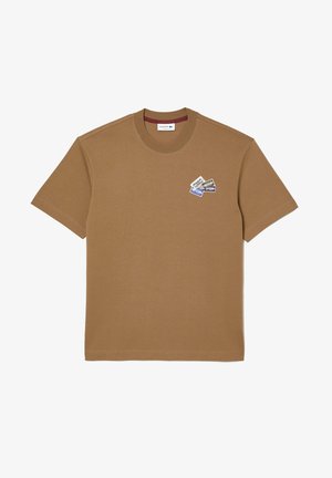 Brązowy t-shirt z krótkim rękawem i okrągłym dekoltem z małymi, wielokolorowymi prostokątnymi naszywkami na lewej piersi.