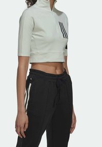 Top corto blanco con mangas cortas, cuello alto y rayas negras laterales, combinado con pantalones joggers negros con acentos blancos laterales y cordón.