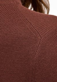 Maglione lavorato a maglia marrone con texture a coste, design delle spalle senza cuciture e tessuto morbido. Vista ravvicinata che mette in evidenza i dettagli delle cuciture.