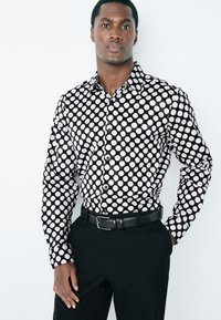 Camicia a maniche lunghe bianca e nera con motivo a pois su tutta la superficie, realizzata in tessuto liscio, abbinata a pantaloni neri e cintura.