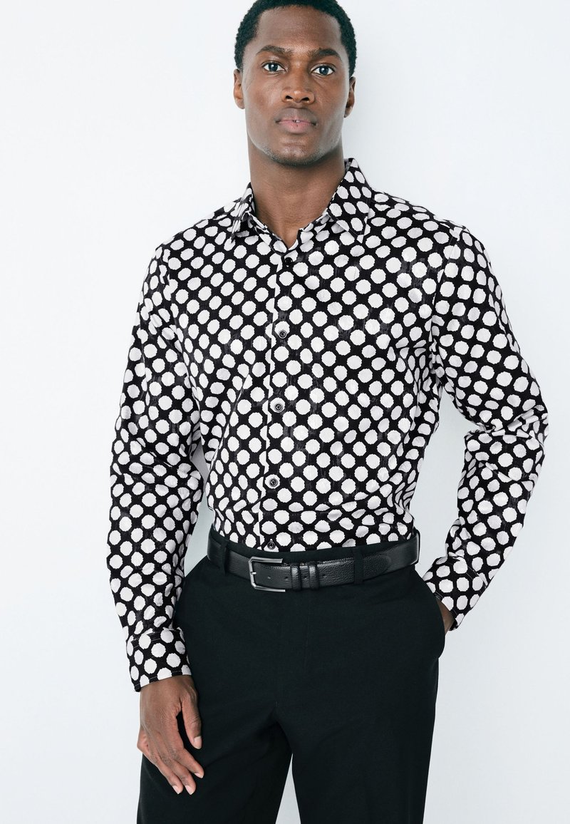 Camicia a maniche lunghe bianca e nera con motivo a pois su tutta la superficie, realizzata in tessuto liscio, abbinata a pantaloni neri e cintura.