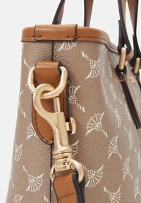 Sac à main beige texturé avec motifs blancs, garniture en cuir marron et quincaillerie dorée. Dispose d'un fermoir doré proéminent et de poignées solides.