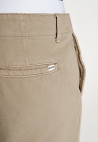 Beige bomuldsbukser med en glat tekstur. Har en baglomme med et lille logomærke og en bælteløkke i taljen.