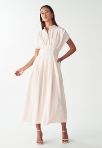Vestido largo de rayas rosas y blancas con mangas cortas abullonadas, cierre de botones y cintura fruncida. Tejido suave con una silueta fluida.