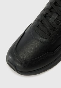 Baskets en cuir noir avec une surface texturée, bout arrondi et lacets plats. Fini lisse avec un design minimaliste et une semelle robuste.