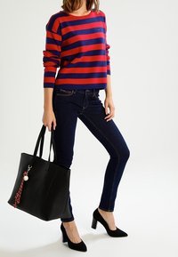 Czerwono-granatowy sweter w paski, czarna skórzana torba z czerwonym akcentem, ciemne obcisłe dżinsy oraz czarne buty na wysokim obcasie.