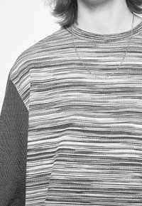 Camiseta a rayas en blanco y negro, con una tela texturizada que presenta diferentes grosores de rayas y un diseño de cuello redondo.