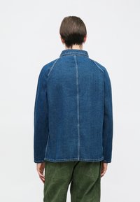 Kurtka jeansowa o przemyślanej konstrukcji, w ciemnoniebieskim kolorze, z widocznymi szwami oraz spiczastym kołnierzem. Posiada prosty krój i boczne rozporki.