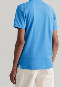 Polo en coton bleu à manches courtes, col côtelé et fentes latérales à l'ourlet, porté avec un pantalon de couleur claire.