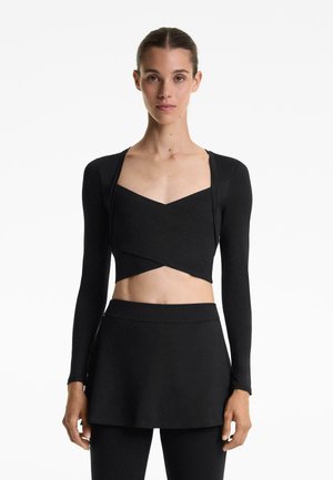 Černý cropped top s dlouhými rukávy, s výstřihem do V a obtočeným designem. Spárován s odpovídající černou sukní, obě vyrobeny z hladké tkaniny.