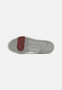 Kumipohjainen tennari, jossa on teksturoitu kuvio, viininpunainen yksityiskohta kantapään lähellä ja Reebok-logo koristeltuna sivussa.