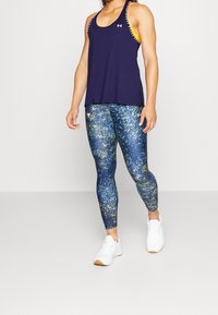 Námořnická atletická tílko s žlutými akcenty, spárované s modrými legínami se zlatým tečkovaným vzorem. Bílé tenisky dotvářejí celý outfit.