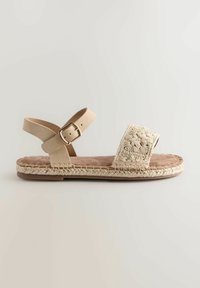 Beige sandaal met een gevlochten jute zool, brede stoffen band met bloemengestikt, en een verstelbare enkelband met een metalen gesp.