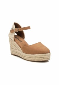 Zapato de cuña de ante color marrón con suela de cuerda de yute, presenta una correa en el tobillo y un acento de tela estampada en el talón. Diseño de puntera redondeada.