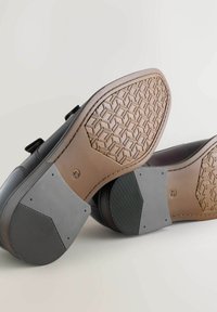 Zwarte schoenen met een glad leren bovenwerk en een getextureerde bruine rubberen zool met een geometrisch patroon,accentueert met grijze rubberen secties.