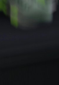 Conteneur en plastique avec un couvercle vert, légèrement translucide, forme rectangulaire, placé sur une surface sombre, peu de texte ou de marquages visibles.