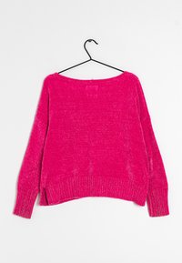 Pull en tricot rose avec un large encolure, des poignets et un ourlet côtelés. Présente des fentes latérales et une finition texturée. Suspendu à un crochet noir.