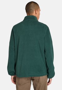 Zielony polarowy sweatshirt z wysokim kołnierzem i długimi rękawami. Posiada miękką teksturę oraz kwadratową metkę z tyłu kołnierza.