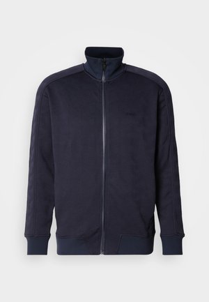 Marineblauwe zip-up jas met hoge kraag, gestructureerd oppervlak met een geometrisch patroon en contrasterende uniforme zoom en mouwen.