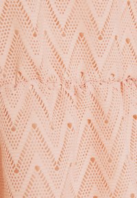 La tela de punto de color rosa claro presenta un patrón en zigzag con pequeños agujeros, creando un aspecto texturizado. El diseño es continuo y suave en general.