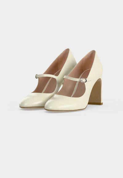 Paire d'escarpins Mary Jane couleur crème à talons hauts avec bouts arrondis et brides à la cheville munies de petites boucles argentées.