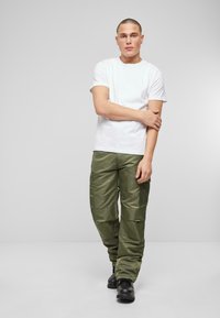 T-shirt blanc à manches courtes associé à un pantalon cargo vert olive. Les pantalons sont dotés de plusieurs poches et d'une coupe ample, complétés par des bottes noires.
