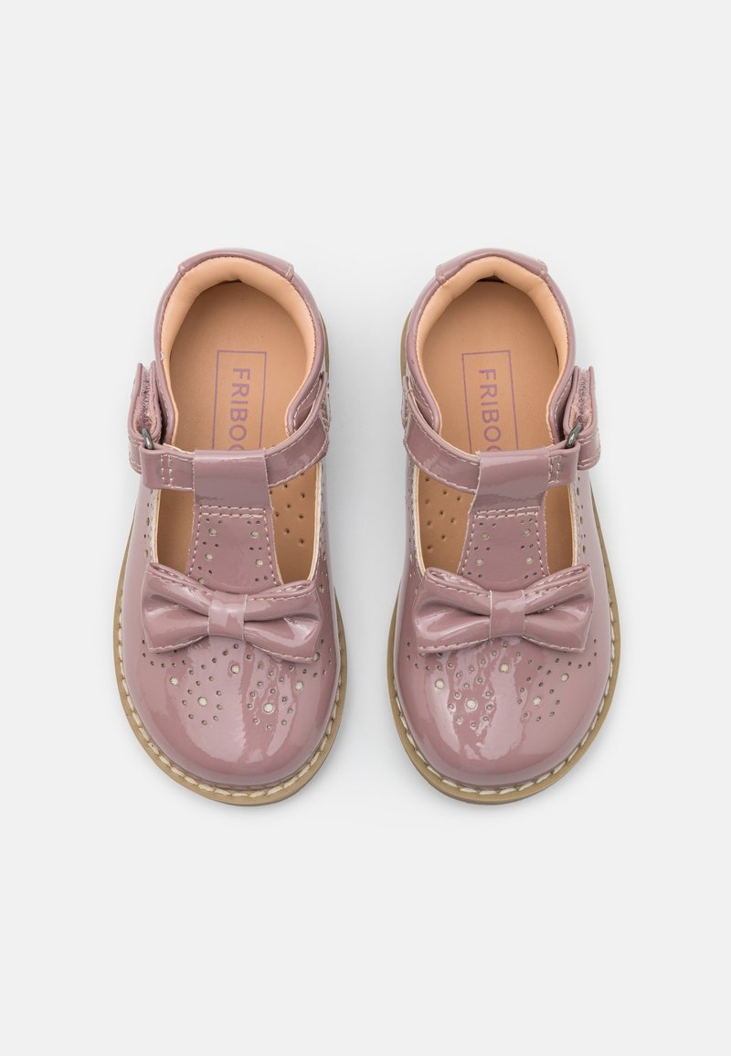 Paire de chaussures roses brillantes pour tout-petits avec détails perforés, nœuds sur le dessus, semelles beiges et brides à la cheville sur fond blanc.