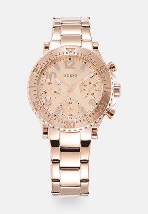 Rose gold analoginen rannekello, jossa on pyöreä kuori, metalliketju-ristikko, kolme alanuolia ja numero-merkinnät vaalealla kellotaululla.