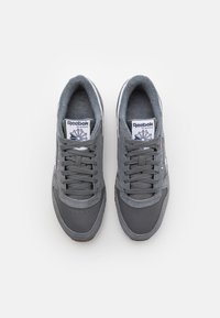 Zapatillas deportivas grises con parte superior de cuero liso y gamuza, puntera redondeada, área de cordones texturizada y el clásico logo de Reebok en la lengüeta.