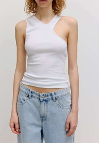 Weißes ärmelloses Oberteil mit asymmetrischem Ausschnitt und glatter Textur, kombiniert mit hellblauen Jeans aus Denim mit heller Ausbleichung und Taschen.