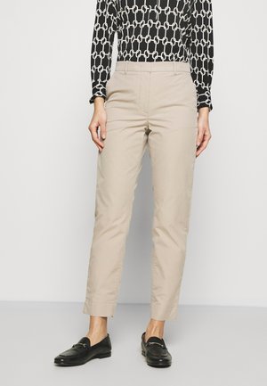 Persoon draagt beige rechte broek, gecombineerd met zwarte loafers en een zwart-wit gebreide top met lange mouwen.