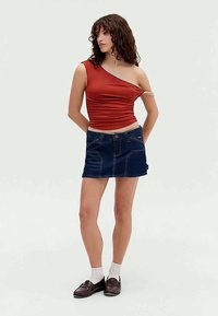 Top rustico monospalla abbinato a una mini gonna in denim scuro. Dettagli notevoli includono una texture arricciata e cuciture in vistose.