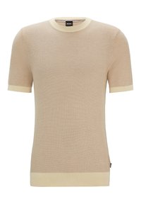 Pull beige à manches courtes en maille avec encolure ras du cou, poignets et ourlet côtelés de couleur beige clair contrastante, avec une étiquette de marque sur le côté.