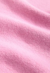 Puha rózsaszín polár anyag enyhén bolyhos textúrával és finom hajtásokkal, amelyek lágy árnyékokat és fényeket hoznak létre.